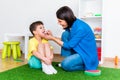 A woman speech therapist deals with a boy and performs an exercise to correct the speech apparatus by playing on the floor