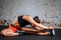 Woman sport stretching in gym with brick wall and black mats