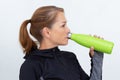 Woman in sportiv dress holding green thermos bottle drinking