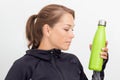 Woman in sportiv dress holding green thermos bottle with water