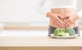 Woman with sports figure on her belly shows heart shape. Fresh broccoli in plate on kitchen table