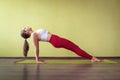 A woman in sportswear does yoga, performs Kumbhakasana exercise, reverse plank pose, trains in a room on a mat near the wall