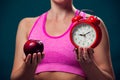 Woman in sportswear holding alarm clock and apple. People, fitness and healthcare concept Royalty Free Stock Photo