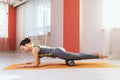 Woman in sportswear performs a myofascial massage of the thigh muscles with a roller on the mat in the gym