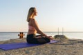 A woman in sportswear, practicing yoga, sitting on a mat in a lotus position, in the evening on the seashore Royalty Free Stock Photo