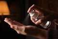 Woman spraying antiseptic onto hand against blurred background, closeup