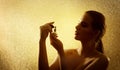 Woman spraying Perfume over Golden Background. Beauty Model Silhouette smelling Luxury Fragrance over Sparkle Curtain. Fashion Royalty Free Stock Photo