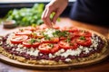 a woman spreading tomato sauce on a cauliflower pizza base