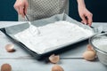 Woman spreads beaten egg whites on a baking sheet covered with parchment on a white vintage wooden table. T