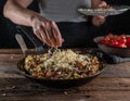 Woman sprinkles cheese over a pan with farmers breakfast. Royalty Free Stock Photo