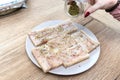 A woman sprinkles lovage on a fresh cod fillet cut into squares, sprinkled with spices.