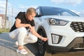 Woman squats down in front of her car and looks at a scratch on the bumper