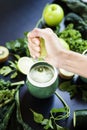 A woman is squeezing a lemon on a green juice of healthy, fresh and raw vegetables on a black background..Kiwi, kale, lemons,