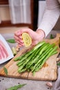 Woman squeezing lime juice onto Green Asparagus on wooden cutting board and slice bacon at kitchen table Royalty Free Stock Photo