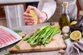 Woman squeezing lime juice onto Green Asparagus on wooden cutting board and slice bacon at kitchen table Royalty Free Stock Photo