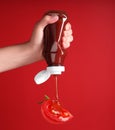 Woman squeezing organic ketchup onto cut tomato against red background, closeup Royalty Free Stock Photo