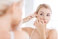 Woman squeezing pimple at bathroom mirror