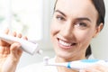 Woman Squeezing Toothpaste Onto Electric Toothbrush In Bathroom