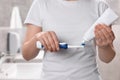 Woman squeezing toothpaste from tube onto electric toothbrush in bathroom, closeup Royalty Free Stock Photo