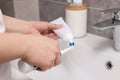 Woman squeezing toothpaste from tube onto toothbrush above sink in bathroom, closeup Royalty Free Stock Photo