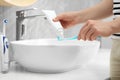 Woman squeezing toothpaste from tube onto toothbrush near sink in bathroom, closeup Royalty Free Stock Photo