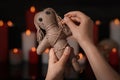 Woman stabbing voodoo doll with pin in dark room, closeup. Curse ceremony