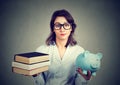 Woman with stack of books and piggy bank full of debt rethinking career path