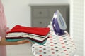 Woman with stack of freshly ironed clothes indoors, closeup