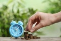 Woman stacking coins and light blue alarm clock on  table, closeup. Money savings Royalty Free Stock Photo