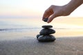 Woman stacking dark stones on sand near sea for text