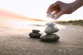 Woman stacking dark stones on sand near sea. Zen concept