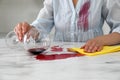 Woman with stain on her shirt cleaning spilled wine from white marble table indoors, closeup