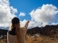 A woman stand in a field of an autumn mountain valley points her finger at the white peak of Elbrus visible behind the