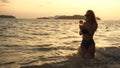 Woman stand knee-deep in sea on sunset. Girl on beach in green swimsuit having fun and waving his hands, drinks her Royalty Free Stock Photo