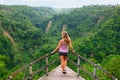 Woman stand on overhanging bridge on high cliff above jungle