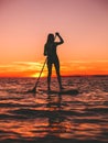 Woman stand up paddle boarding at dusk on a flat warm quiet sea with beautiful sunset Royalty Free Stock Photo