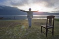 Woman standing alone on the ground, hands raise with open arms against the light over the lake. Royalty Free Stock Photo