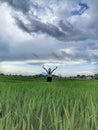 Woman standing alone in the green field with arms raised against dramatic blue sky. Worship and gratefulness concept.