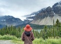 Woman standing backward enjoying the view of mountains and trees covered in clouds.