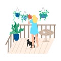 Woman standing on balcony with cat and watering hanging flowers in pots Royalty Free Stock Photo