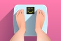 Feet of woman standing on bathroom scales with happy face on display