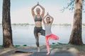 Woman is standing behind her student. They are standing at the river shore and excercising. They are holding hands above