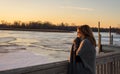 Woman standing on bridge over frozen river watching sunset Royalty Free Stock Photo