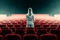 woman standing facing back between seats in empty theater hall, copy space