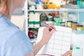 Woman Standing In Front Of Refrigerator In Kitchen With Notebook Writing Weekly Meal Plan