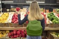 Woman standing in front of a row of produce in a grocery store, holding pepper and shopping at supermarket