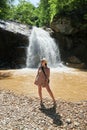 woman standing in front of the waterfall in front of a small path, in the style of beige, sublime wilderness, dry wit humor,