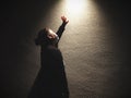 A woman standing with hand reaching the light in the dark. Royalty Free Stock Photo