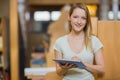 Woman studying in library tapping tablet screen by wooden study carrels and bookshelves, copy space Royalty Free Stock Photo