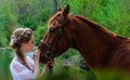 Woman standing with horse near lake and touching horse face with her forehead